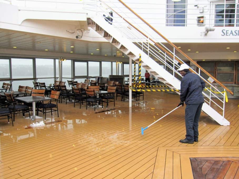Crew member shoveling snow on Celebrity Constellation pool deck in Canada.
