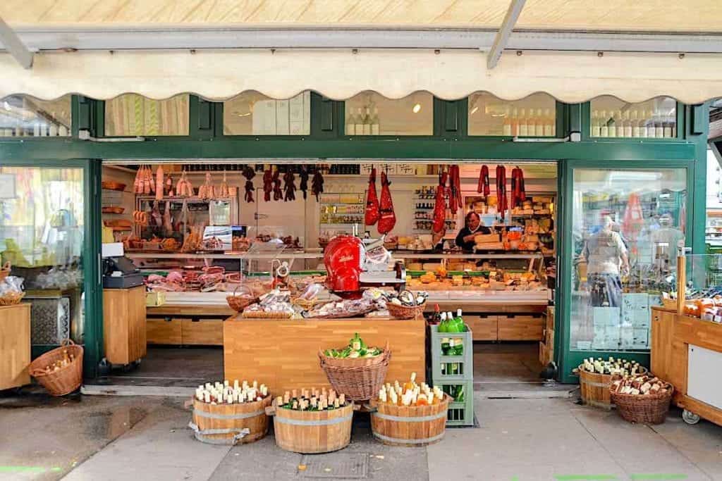 Market with hanging hams and a case of cheeses. 